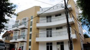 Un immeuble à plusieurs étages doté de balcons, une moto garée et un véhicule utilitaire.