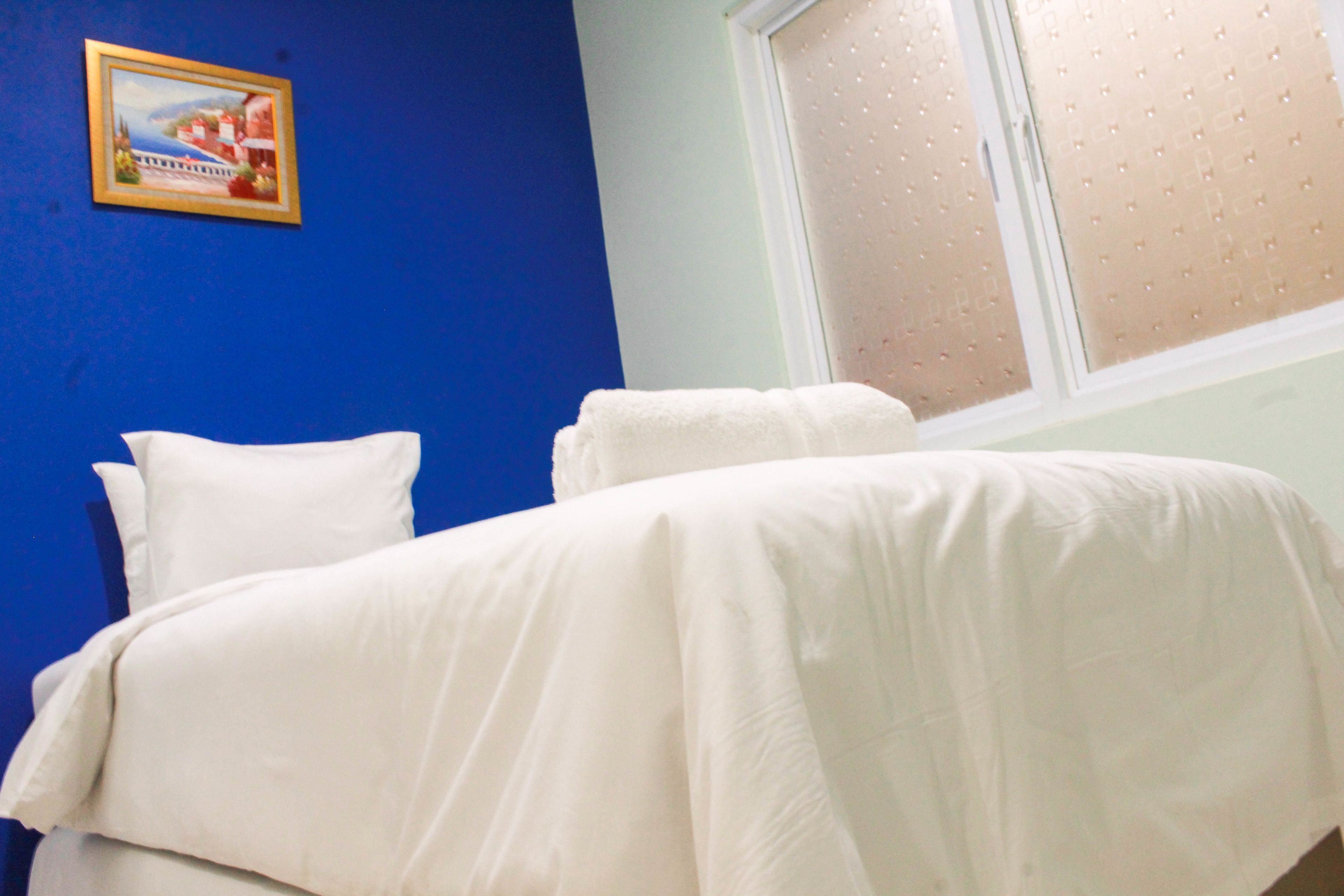 A bedroom with two beds, a blue wall, and a window with blinds.