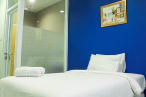 Ein Hotelzimmer mit einem Bett, einem weißen Handtuch, einer blauen Wand und einem gerahmten Bild.