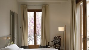 Een hotelkamer met een bed, een stoel, een lamp en een raam met gordijnen.