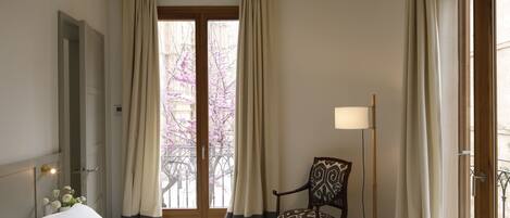 A hotel room with a bed, a chair, a lamp, and a window with curtains.