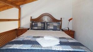 Un dormitorio con cabecera de madera, colcha acolchada, dos mesitas de noche y una mesita de noche con lámpara.