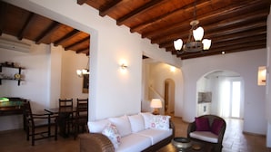 A spacious living area with a wooden ceiling, a sofa, a chair, and a dining table. - Villa Attalus 3 (Mykonos)