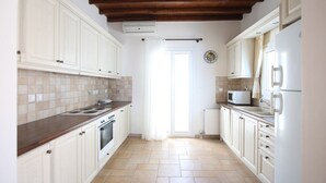 A kitchen with white cabinets, a stove, a microwave, and a refrigerator. - Villa Attalus 3 (Mykonos)