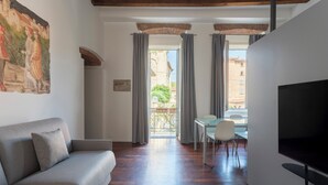 Una sala de estar moderna con sofá, una mesa de comedor con sillas, televisor y balcón con cortinas.