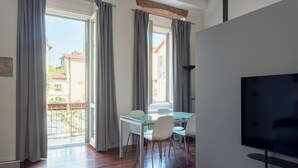 Una sala de estar moderna con comedor, ventanas amplias con cortinas, televisor de pantalla plana y balcón con vistas a edificios.