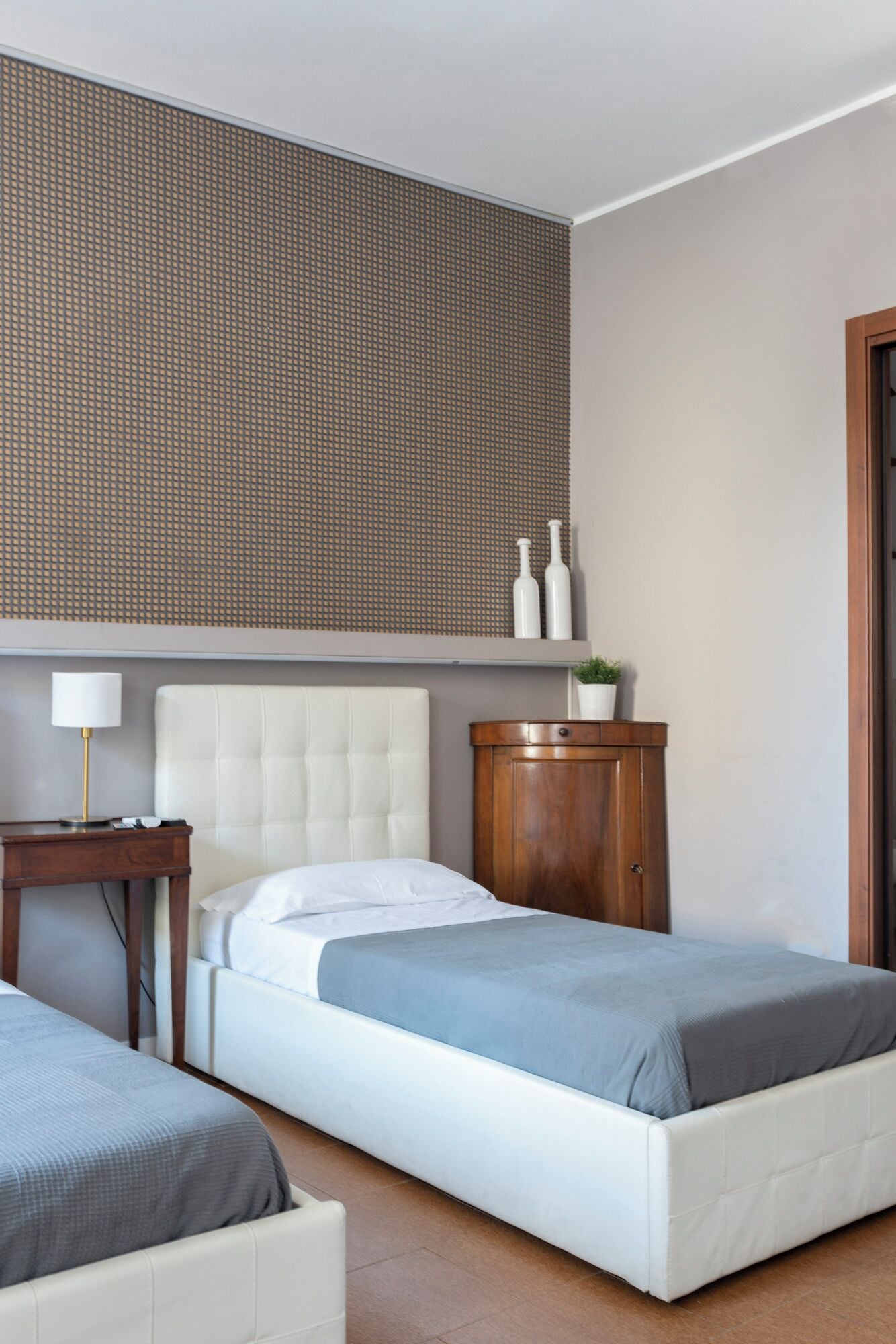 Une chambre d’hôtel avec un lit simple, une table de chevet avec une lampe, une armoire en bois et un panneau mural texturé.
