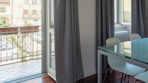 Una habitación con balcón, una mesa de comedor y cortinas grises.