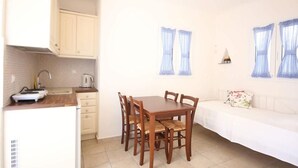Una cocina compacta con una mesa de comedor y sillas, un pequeño sofá blanco y una ventana con cortinas.