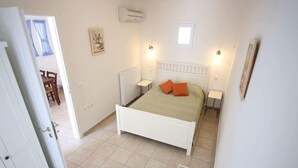 Un dormitorio con una cama blanca, dos mesitas de noche, un radiador y un ventanal pequeño.