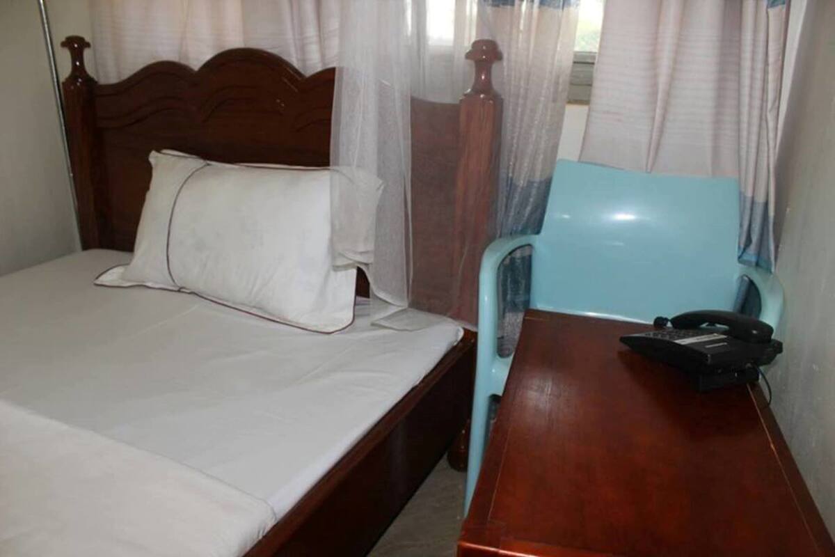 A single bed with a wooden headboard, a bedside table with a telephone, and a light blue chair.