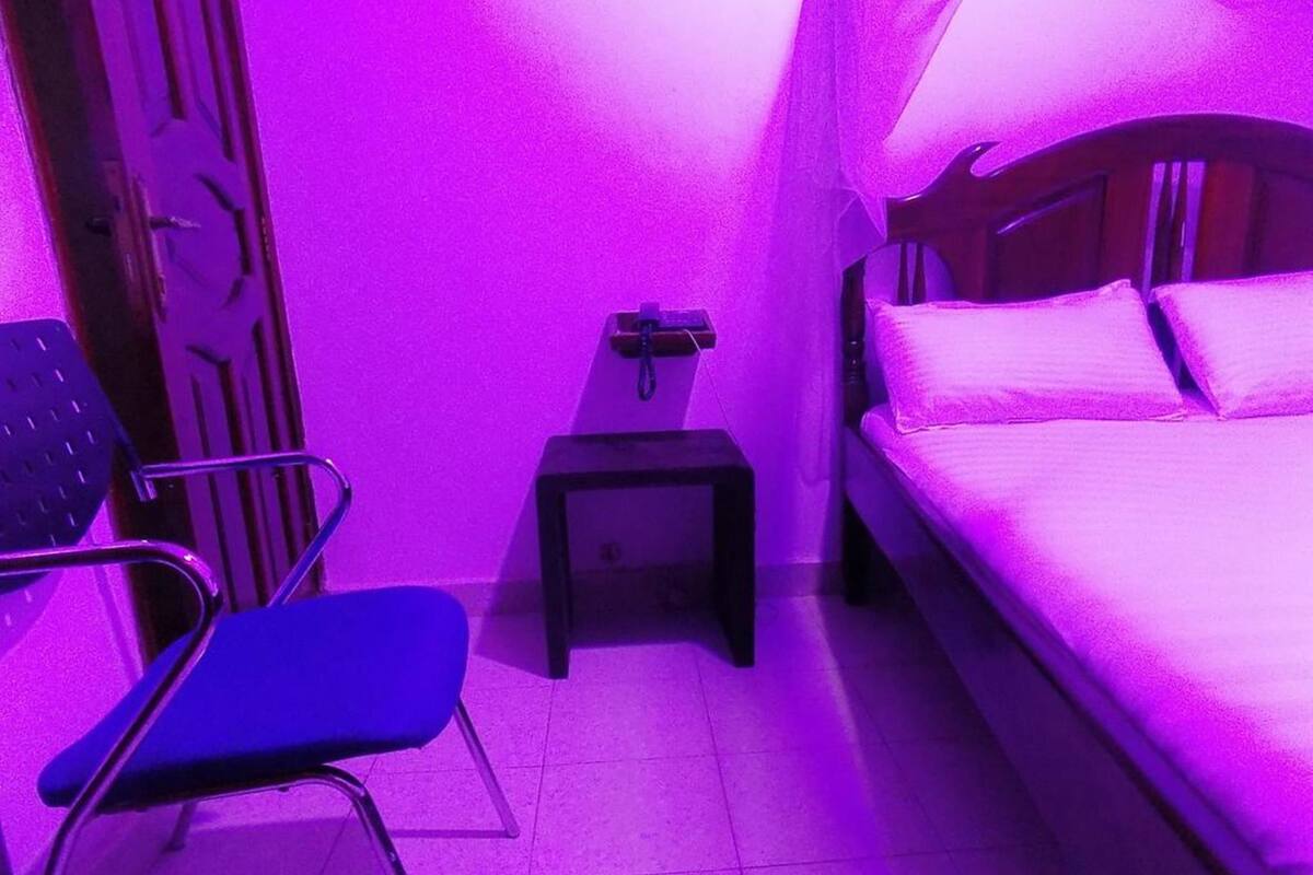 A small, narrow room with a bed, a chair, a nightstand, and a door.