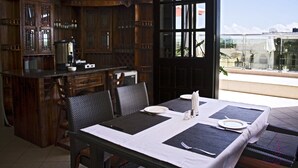 A dining area with a table set for two, wooden cabinetry, and a view through a large window. - Island Paradise Apartment (Zanzibar Town)