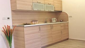 Eine kleine Küche mit hellem Holzkorpus, einer weißen Arbeitsplatte und einem Edelstahl-Spülbecken.