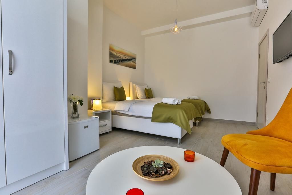 A modern hotel room with a bed, bedside tables, a small table with a bowl and candle, and a yellow chair.