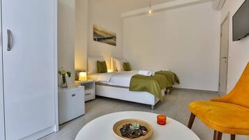 A modern hotel room with a bed, bedside tables, a small table with a bowl and candle, and a yellow chair.