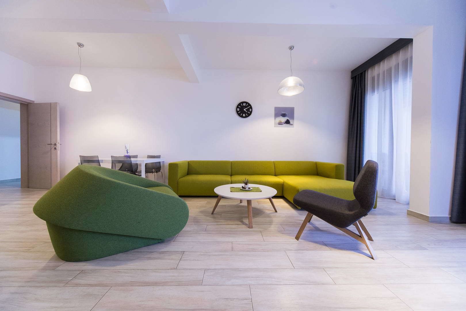 A modern living room with a green sofa, a round coffee table, and a black armchair. There is a dining area in the background with a white table and chairs.