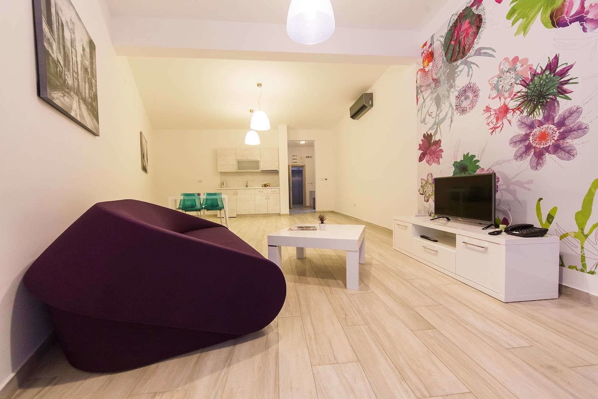 A modern living room with a purple sofa, a white coffee table, and a TV on a white cabinet.