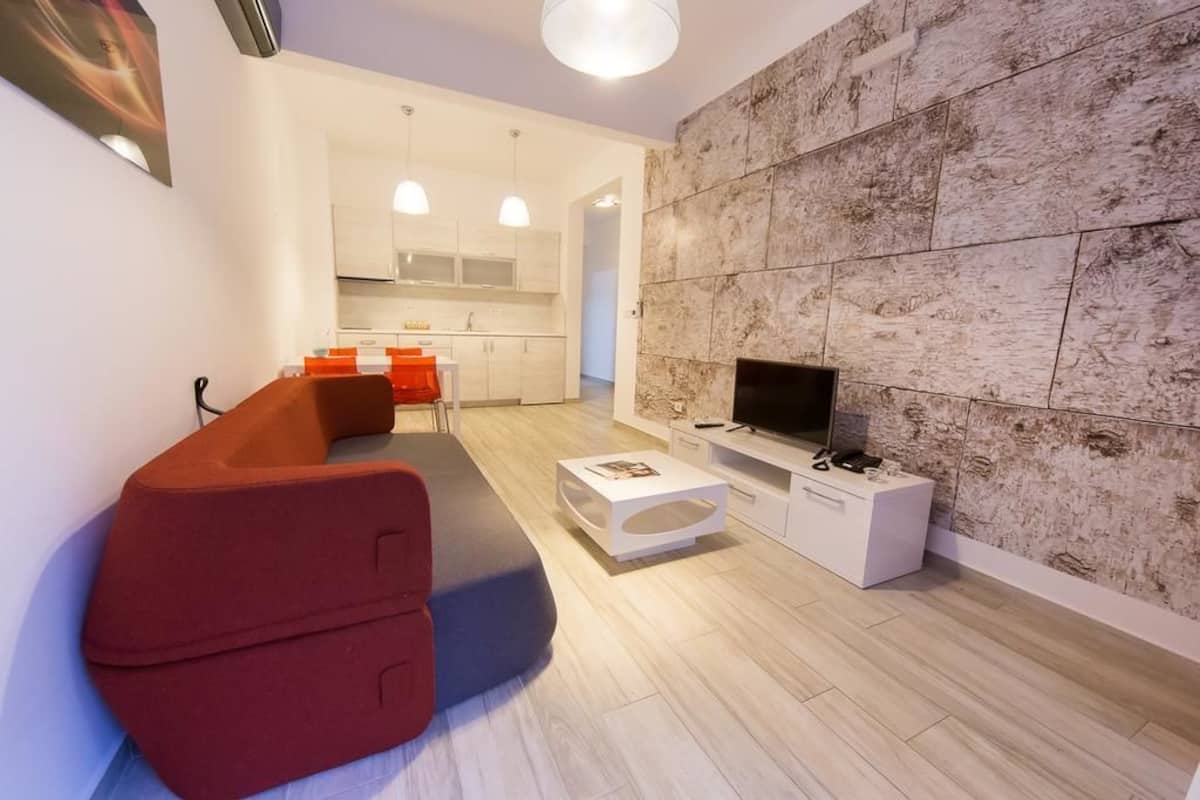 A modern living room with a red sofa, a flat-screen TV, and a stone-textured wall.