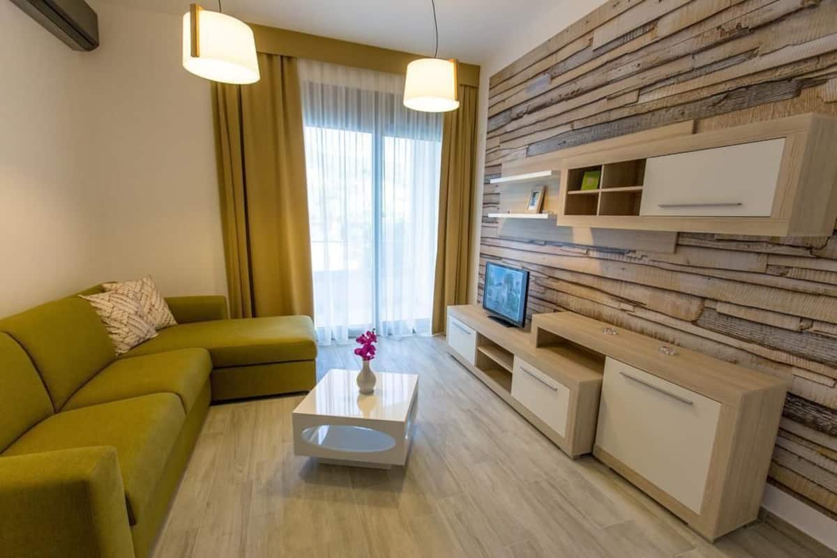 A modern living room with a green sofa, a white coffee table, and a wooden wall with built-in shelves and a TV.