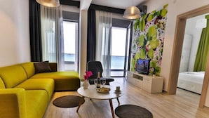 A modern living room with a yellow sofa, a round coffee table, and a television on a stand. - Apart Hotel Sea Fort (Sutomore)