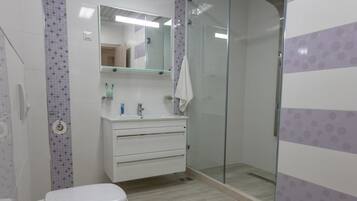 Un baño con inodoro, lavabo con espejo y cabina de ducha con mampara de vidrio.