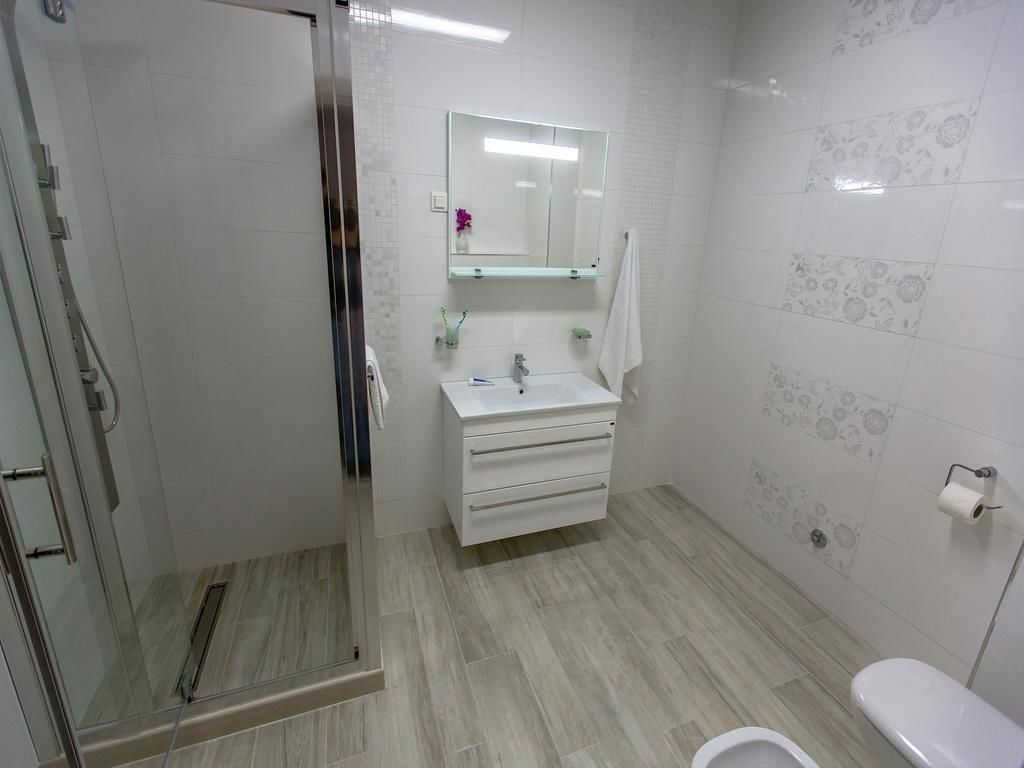 A bathroom with a glass shower enclosure, a white sink with a mirror above it, and a toilet.