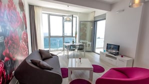 A modern living room with a sofa, a coffee table, and a TV. There is a balcony with a view of the sea. - Apart Hotel Sea Fort (Sutomore)