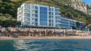 A modern hotel with multiple floors, a beachside location, and numerous beach umbrellas. - Apart Hotel Sea Fort (Sutomore)