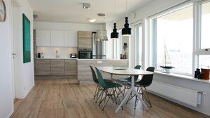 A modern kitchen with a dining area, wooden flooring, and large windows. - Nest Apartment Sparrow (Reykjavik)