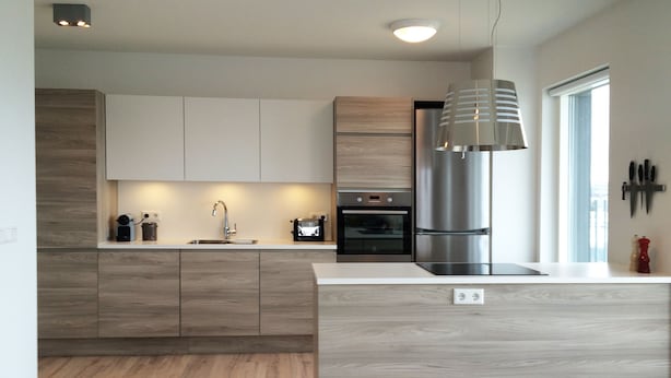 A modern kitchen with wooden cabinetry, a stainless steel refrigerator, and a built-in oven. - Nest Apartment Sparrow (Reykjavik)