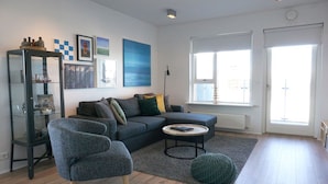 A modern living room with a sectional sofa, a round coffee table, and a glass cabinet. - Nest Apartment Sparrow (Reykjavik)