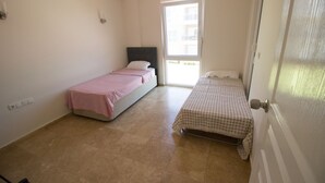 Una habitación pequeña y luminosa con dos camas individuales, una puerta y un ventanal.