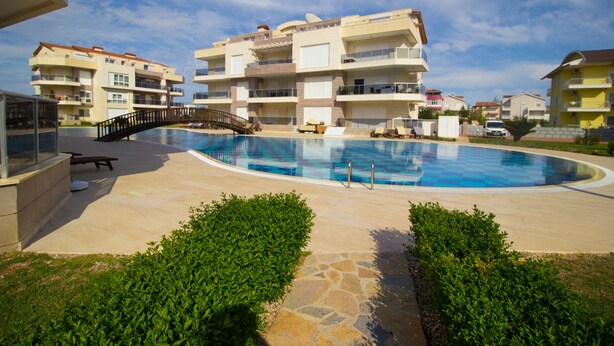 Una piscina rodeada de edificios de apartamentos con balcones, un puente y un sendero de piedra.