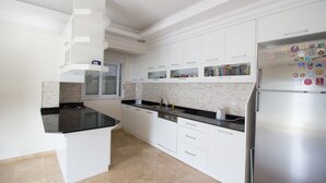 Una cocina moderna con armarios blancos, encimera negra y refrigerador de acero inoxidable.