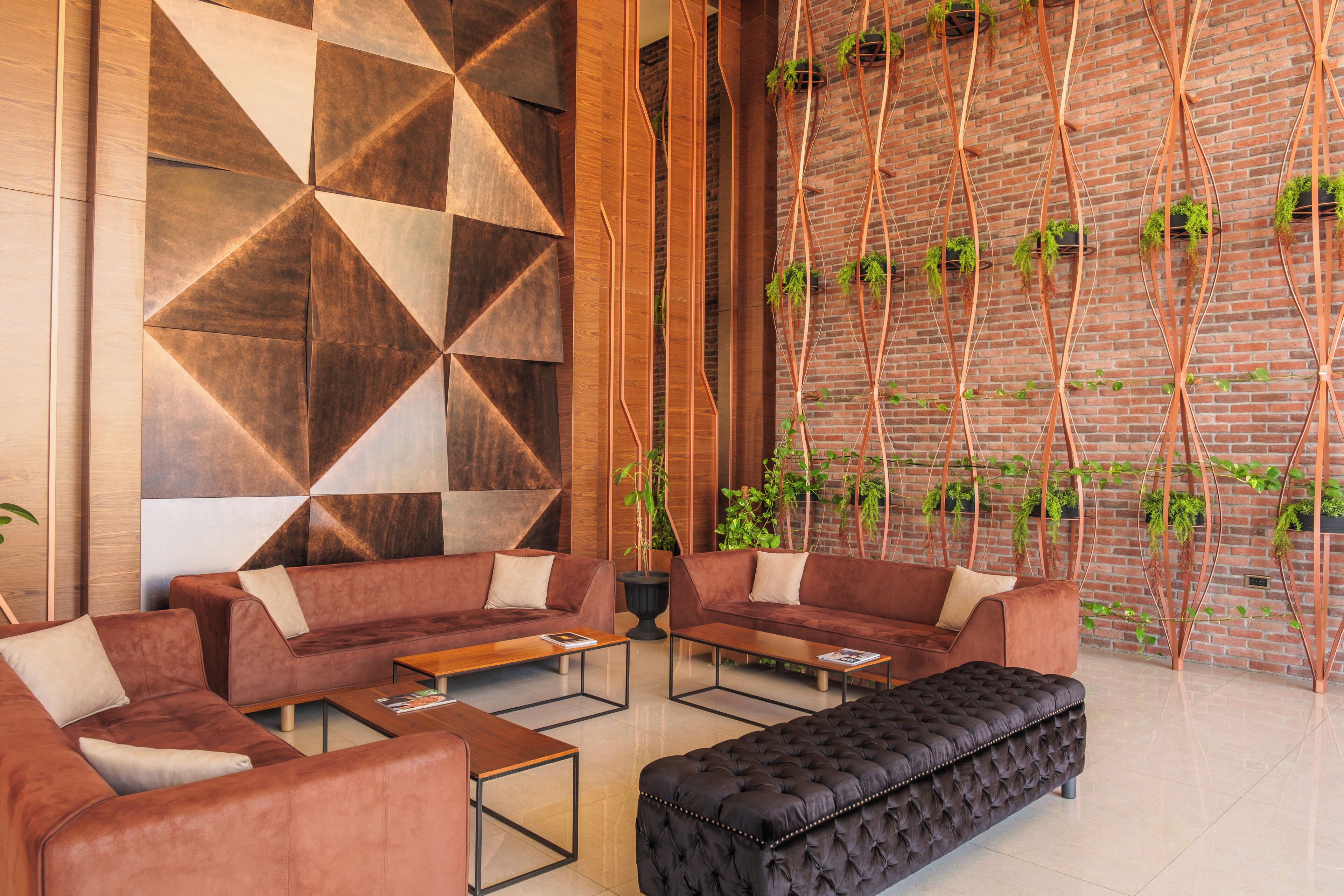 Un intérieur moderne avec un motif géométrique sur un mur, des canapés en cuir, un pouf noir à capitons et un mur en briques orné de plantes suspendues.