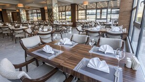 A modern restaurant with multiple dining tables set for guests, featuring a mix of wooden and upholstered chairs. - Shimall Deluxe Hotel (Gaziantep)