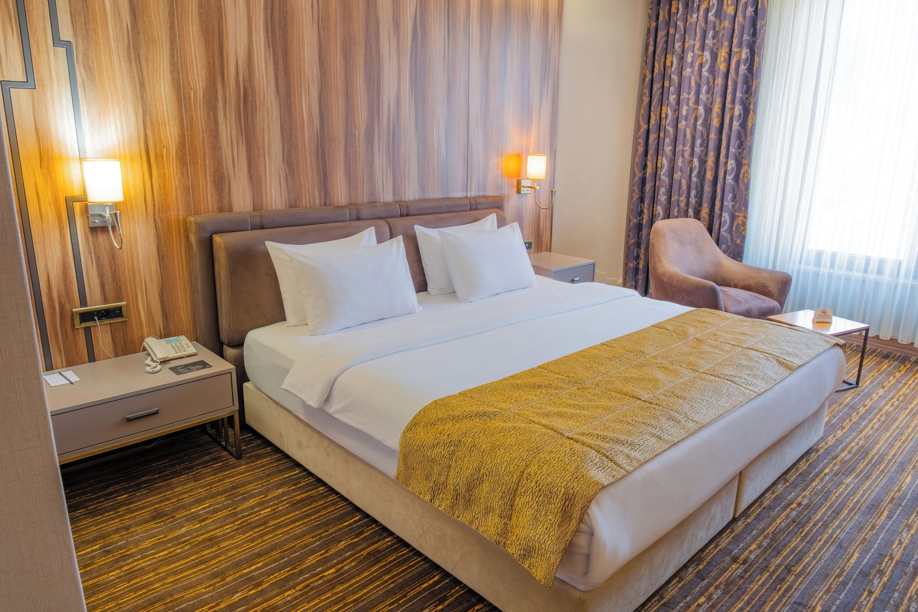 Ein Hotelzimmer mit einem großen Bett, Nachttischen, einem Sessel und einem Holz-Kopfteil.