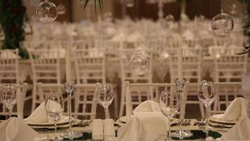 Un salón de banquetes con mesas dispuestas para un evento formal, destacando manteles blancos, copas y velas.