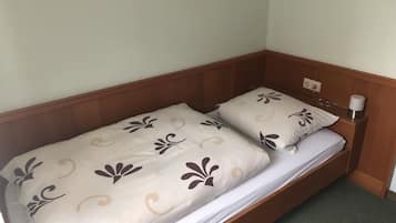 Een enkel bed met een houten hoofdeinde, twee kussens met een bloemenmotief en een nachtkastje met een lamp.