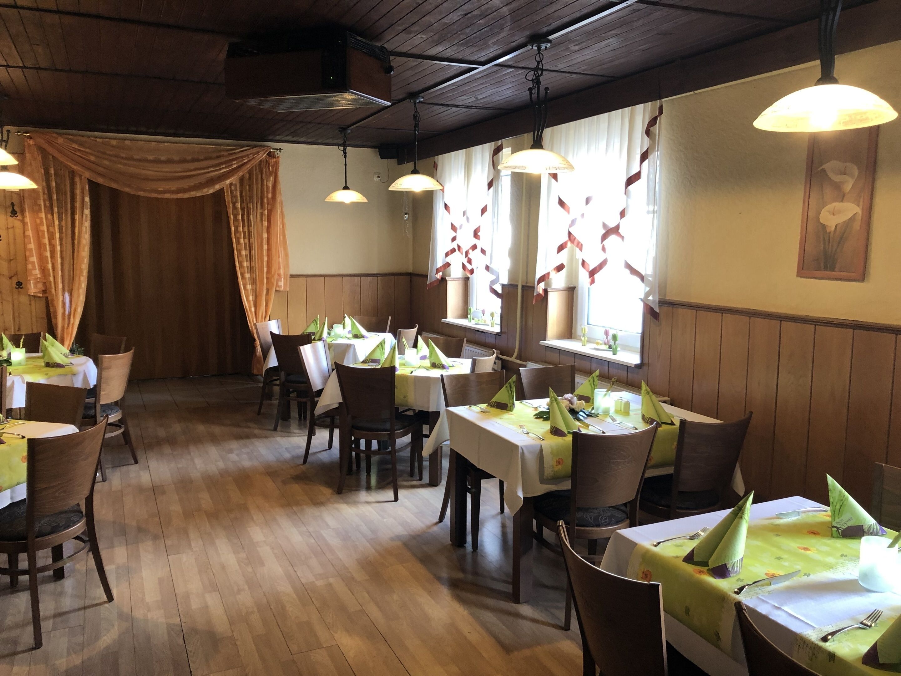 A restaurant with wooden floors and tables set with green tablecloths and napkins.