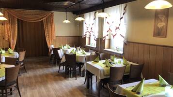 A restaurant with wooden floors and tables set with green tablecloths and napkins.