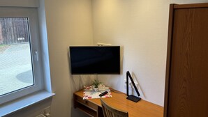 Une pièce avec un bureau en bois, un téléviseur fixé au mur, une fenêtre et une porte.