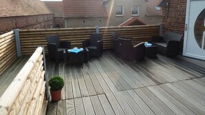 Une terrasse sur le toit avec un plancher en bois, des meubles en osier et une plante en pot.