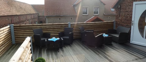 A rooftop patio with wooden flooring, wicker furniture, and a potted plant.