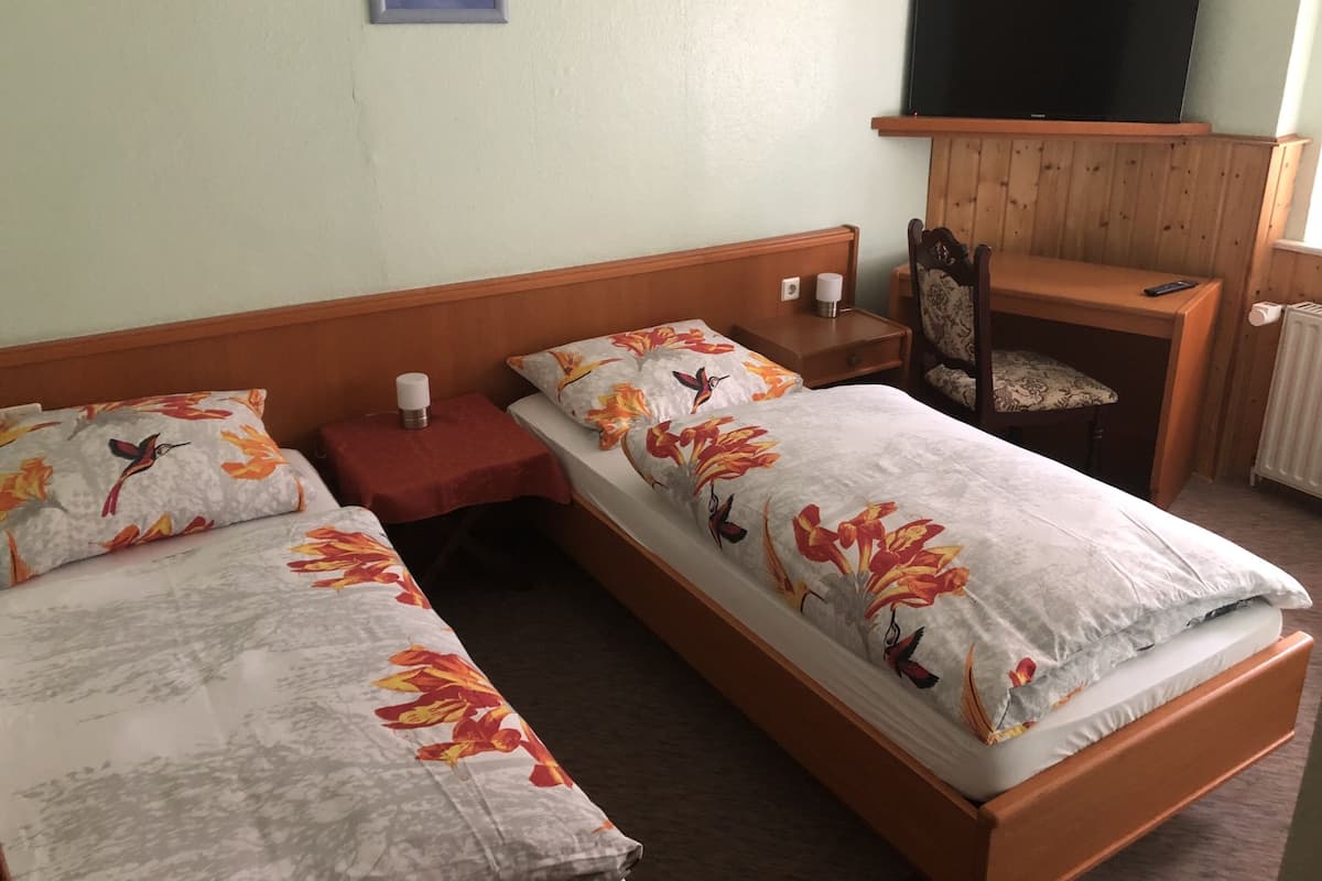 A double bed with floral bedding, a bedside table with a lamp, a chair, a TV on a wooden stand, and a radiator.