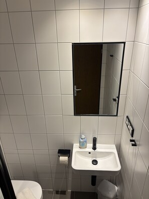 Une petite salle de bain moderne avec des carreaux blancs, un lavabo blanc, un miroir et des toilettes.