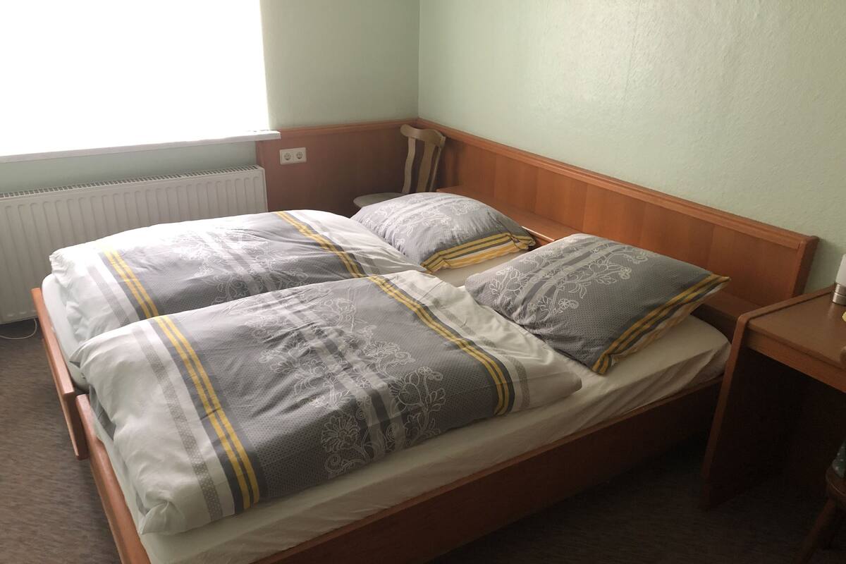 A double bed with a wooden frame, two pillows with a floral pattern, and a bedside table with a lamp.