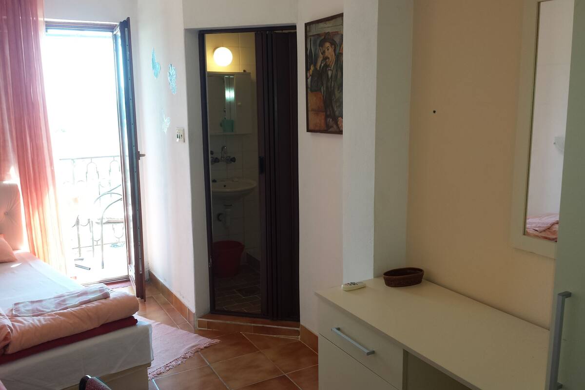 A bedroom with a bed, a bedside table, a dresser, and a bathroom visible through an open door.