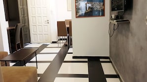 Un vestíbulo de hotel con piso a cuadros, una zona de comedor con sillas y mesas, y un televisor montado en la pared.